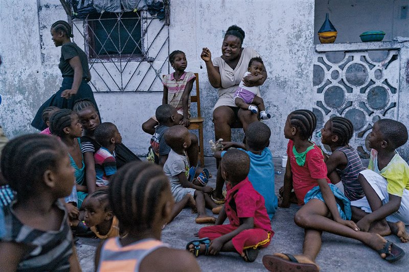 Los niños se sientan en torno a Patience Brooks, que tiene en el regazo a su benjamina, Marta, en Mamba Point, un barrio de Monrovia. Madres y niños del barrio se turnan para contar cuentos mientras preparan las cenas familiares.