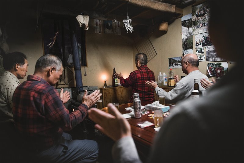 La media de edad de los cazadores matagi oscila entre los 60 y 70 años. Finalizada la cacería, los hombres se reúnen bajo el techo de su capitán, Takeshi Sato, para dar comienzo al ritual que precede a la cena en comunidad. Haruo Endo oficia el rezo frente al corazón del oso y una botella de sake.