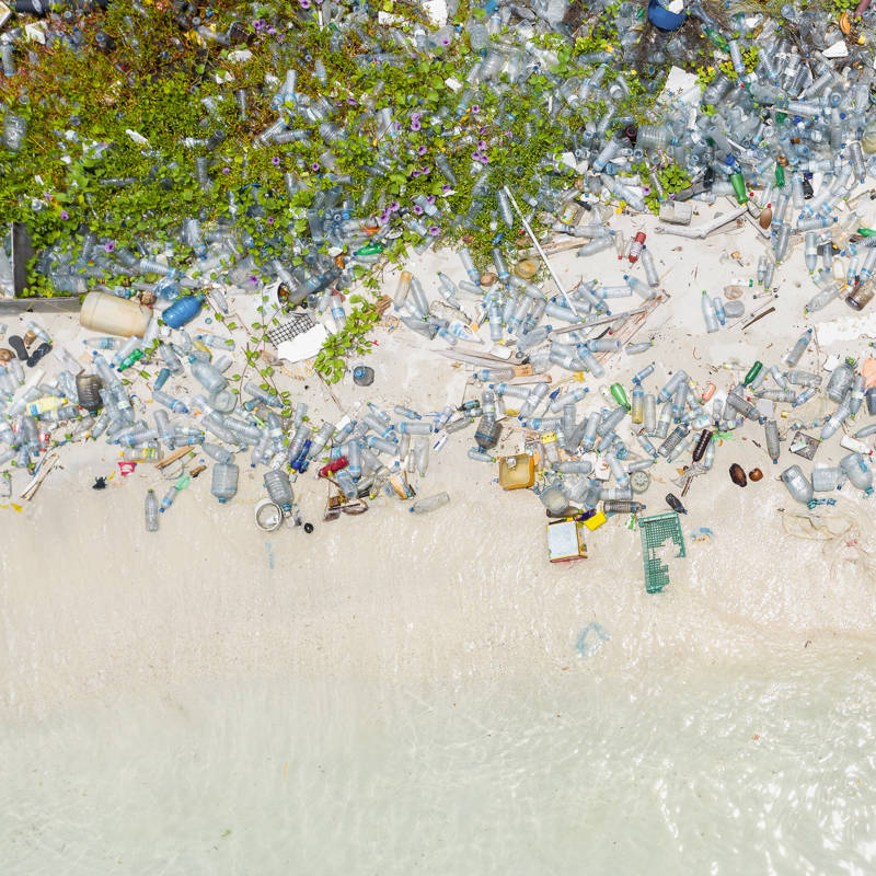 Vista aérea de montones de botellas de plástico y otros tipos de residuos de plástico lavados en una playa de arena tropical