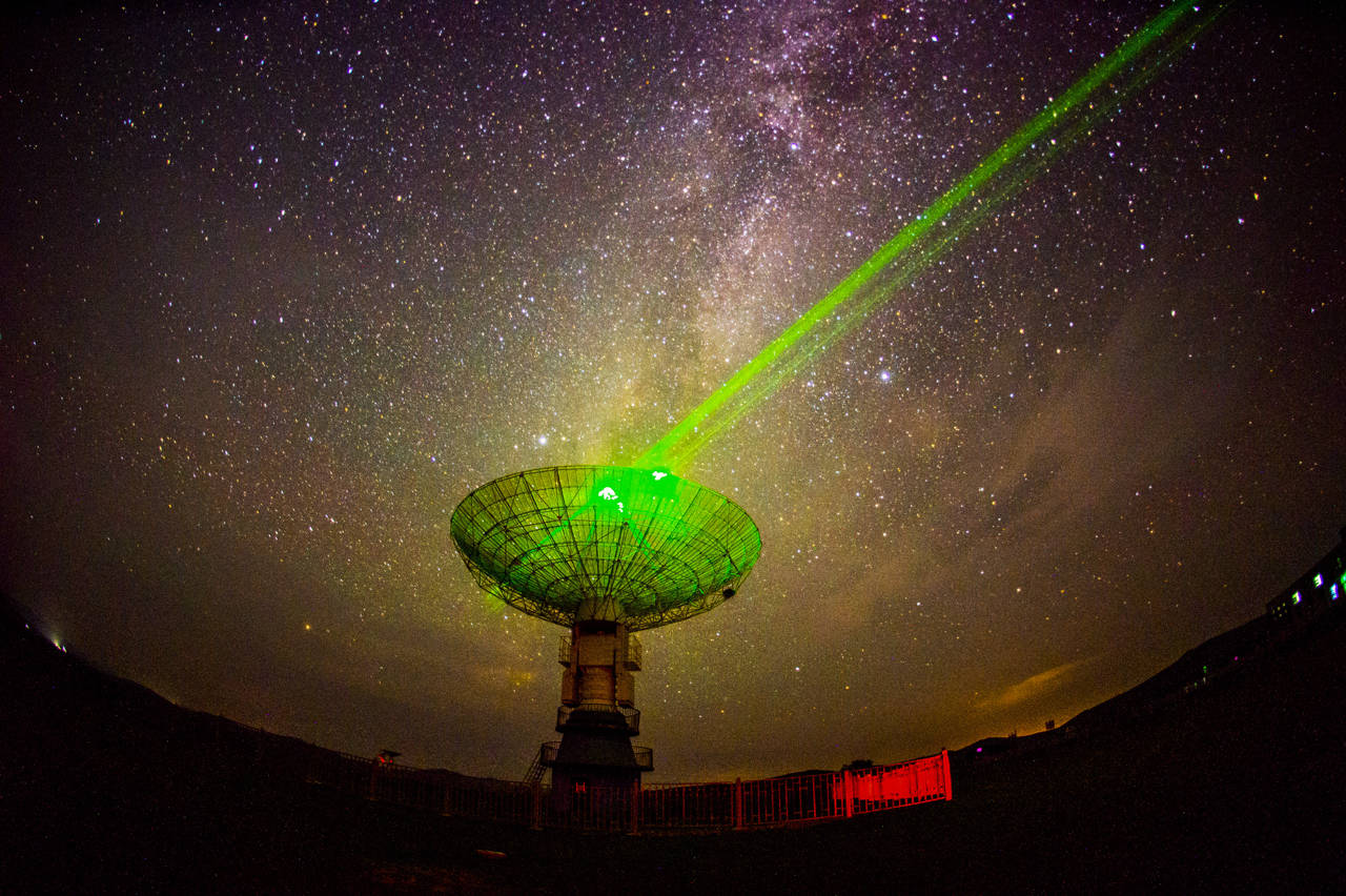 Un radiotelescopio con una imagen de la Vía Láctea de fondo