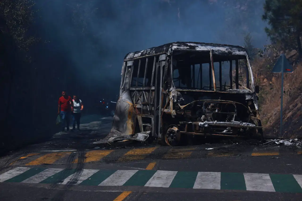Los peatones pasan junto a un vehículo calcinado tras ser incendiado, en una carretera de Cointzio, estado de Michoacán, México, el domingo 22 de febrero de 2026.